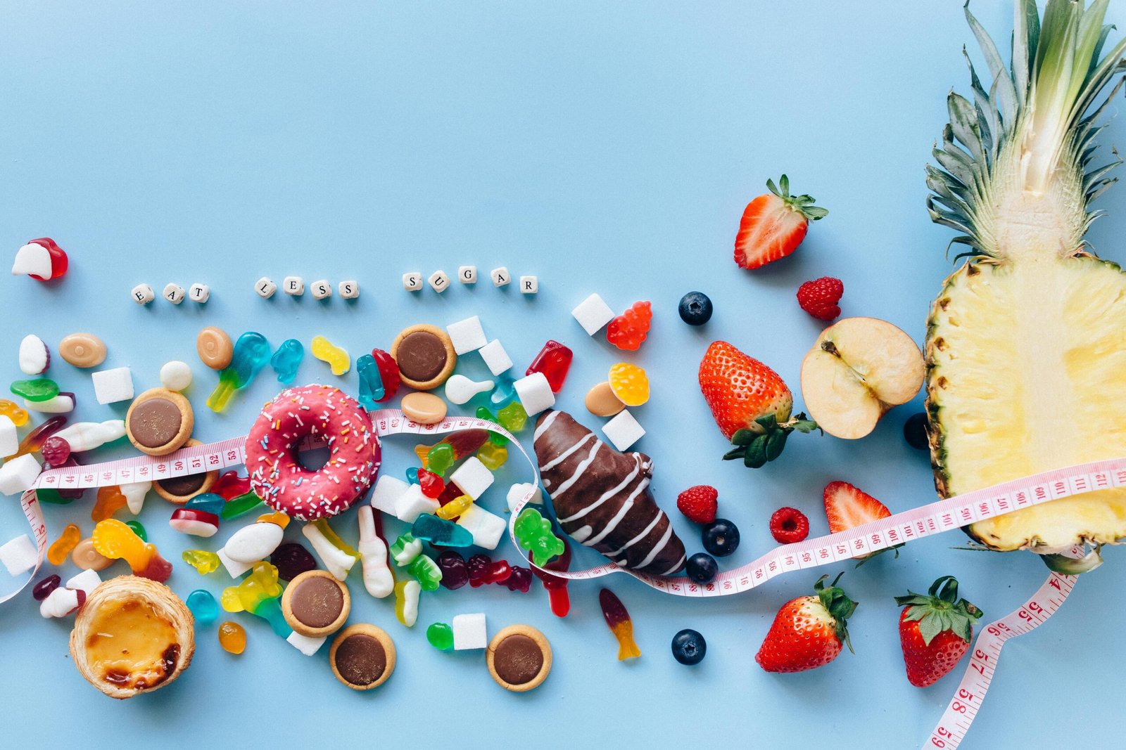 Flat lay of sweets and fruits on blue background with health message 'Eat Less Sugar'.